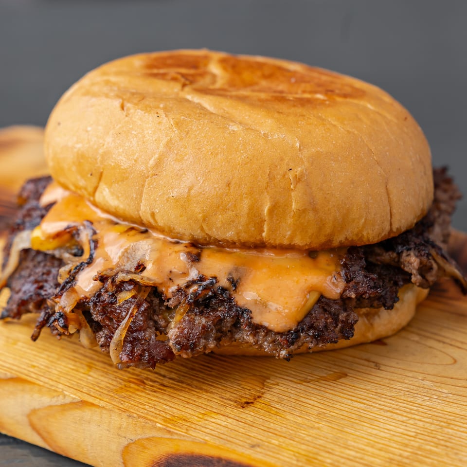 Close-up of a juicy double cheeseburger with melted cheese and grilled onions on a wooden board.