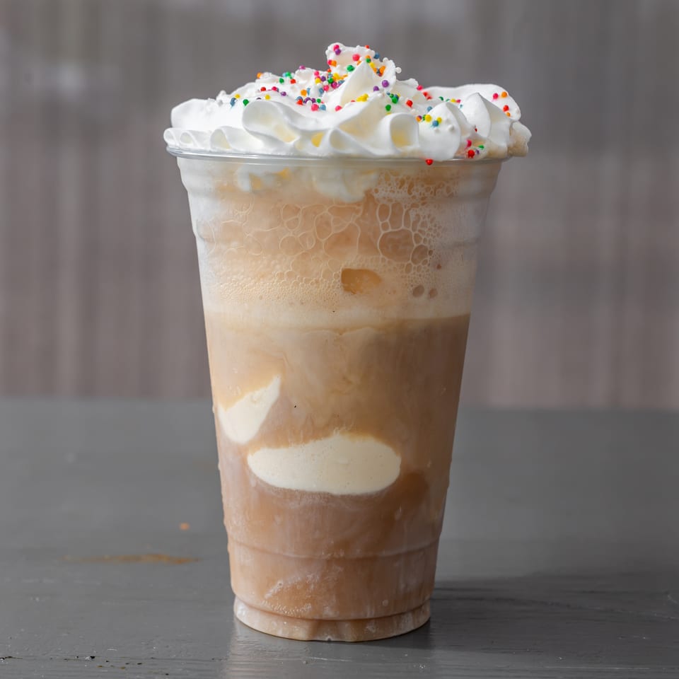 Iced coffee in a clear cup topped with whipped cream and colorful sprinkles.