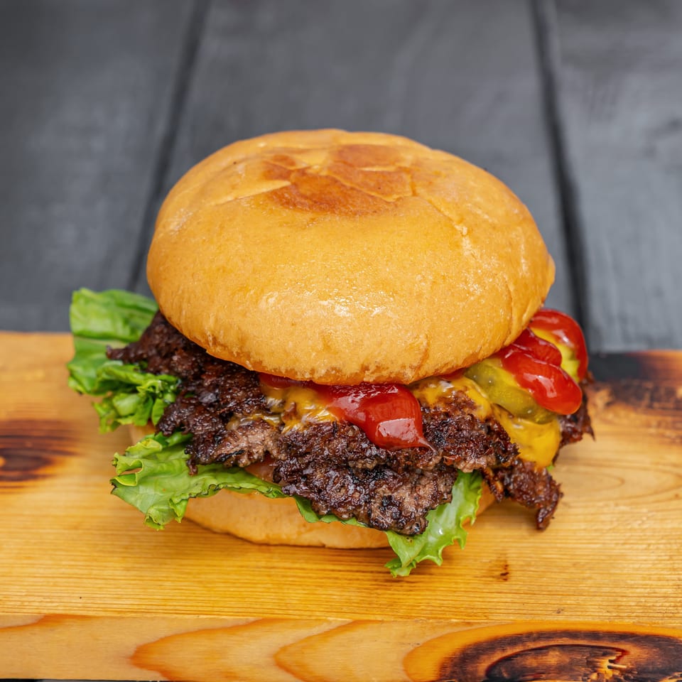 Double cheeseburger with lettuce, tomatoes, pickles, and ketchup on a wooden board.