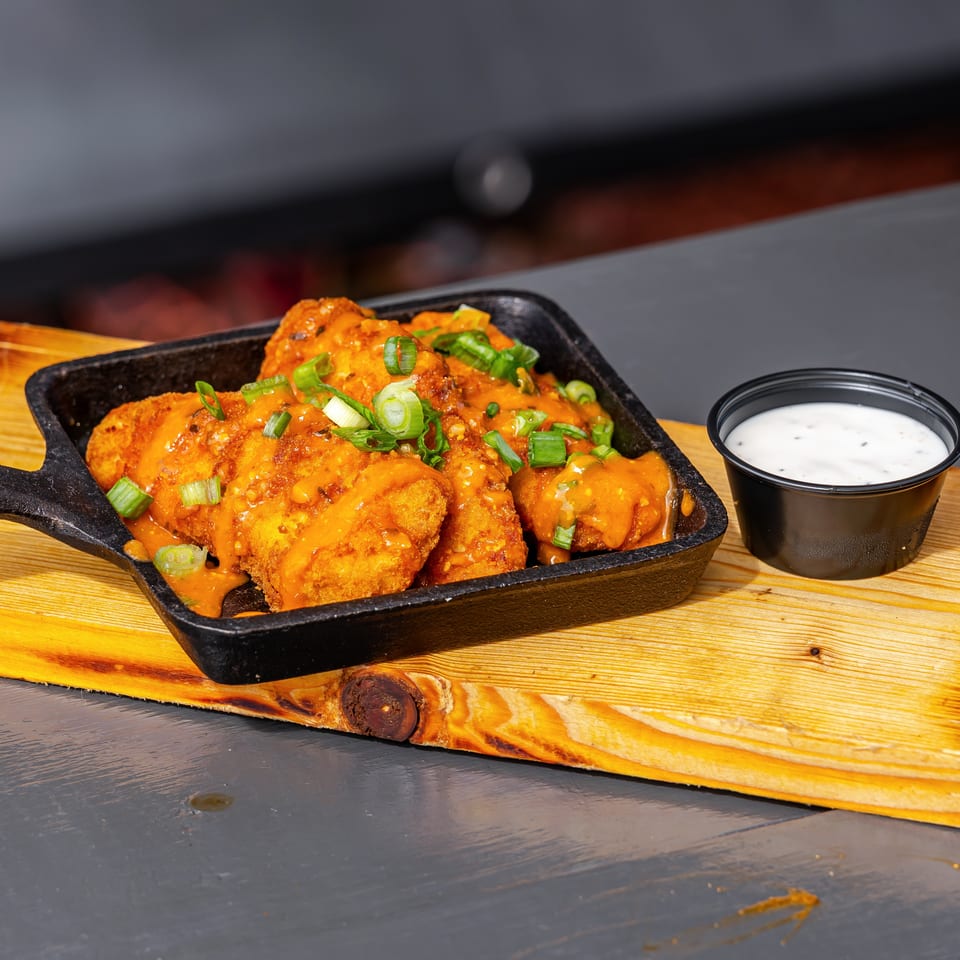 Crispy fried bites covered in orange sauce and green onions, served in a cast-iron dish with ranch dipping sauce.