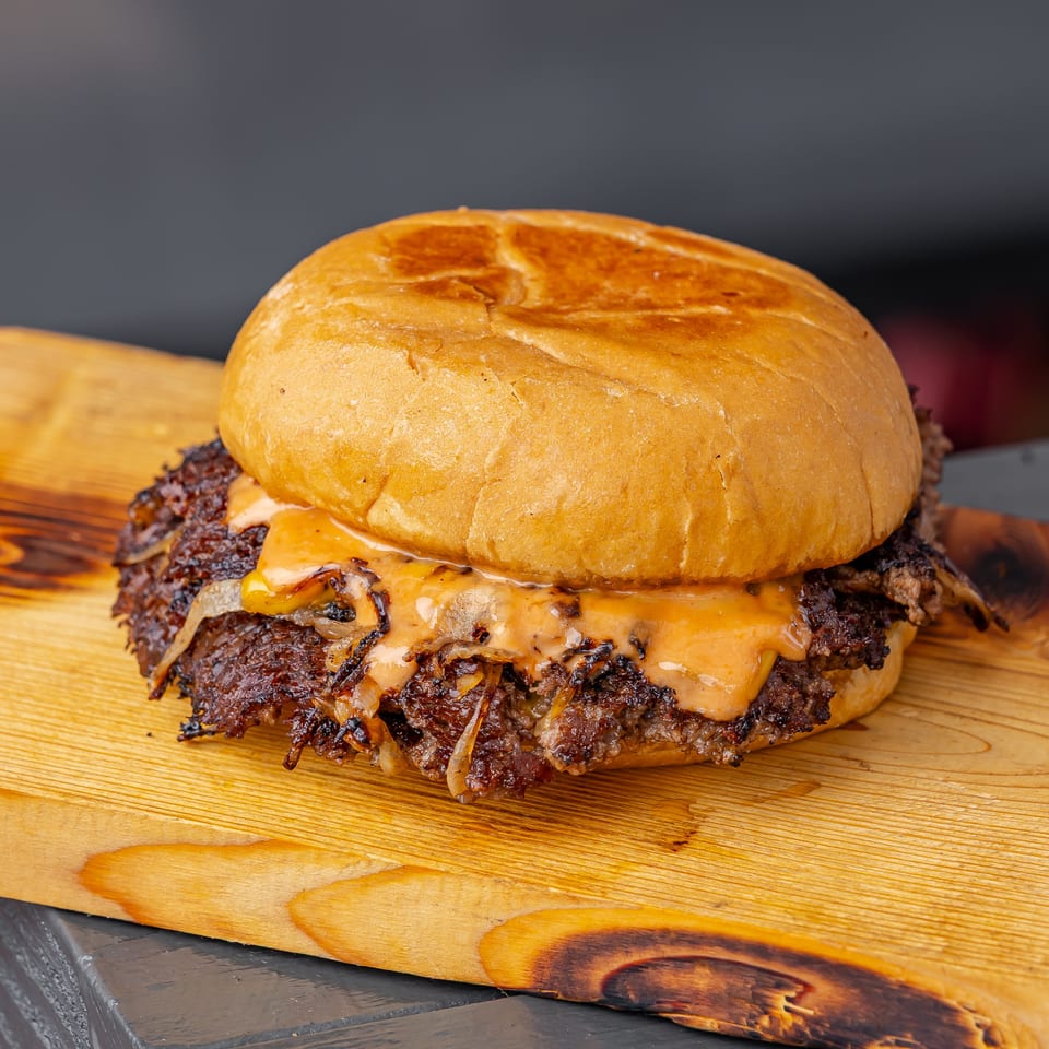 Close-up of a cheeseburger with a toasted bun, crispy beef patty, melted cheese, and grilled onions on a wooden board.