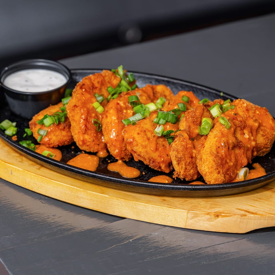 Crispy orange-sauced fried chicken topped with green onions, served on a black platter with dipping sauce.