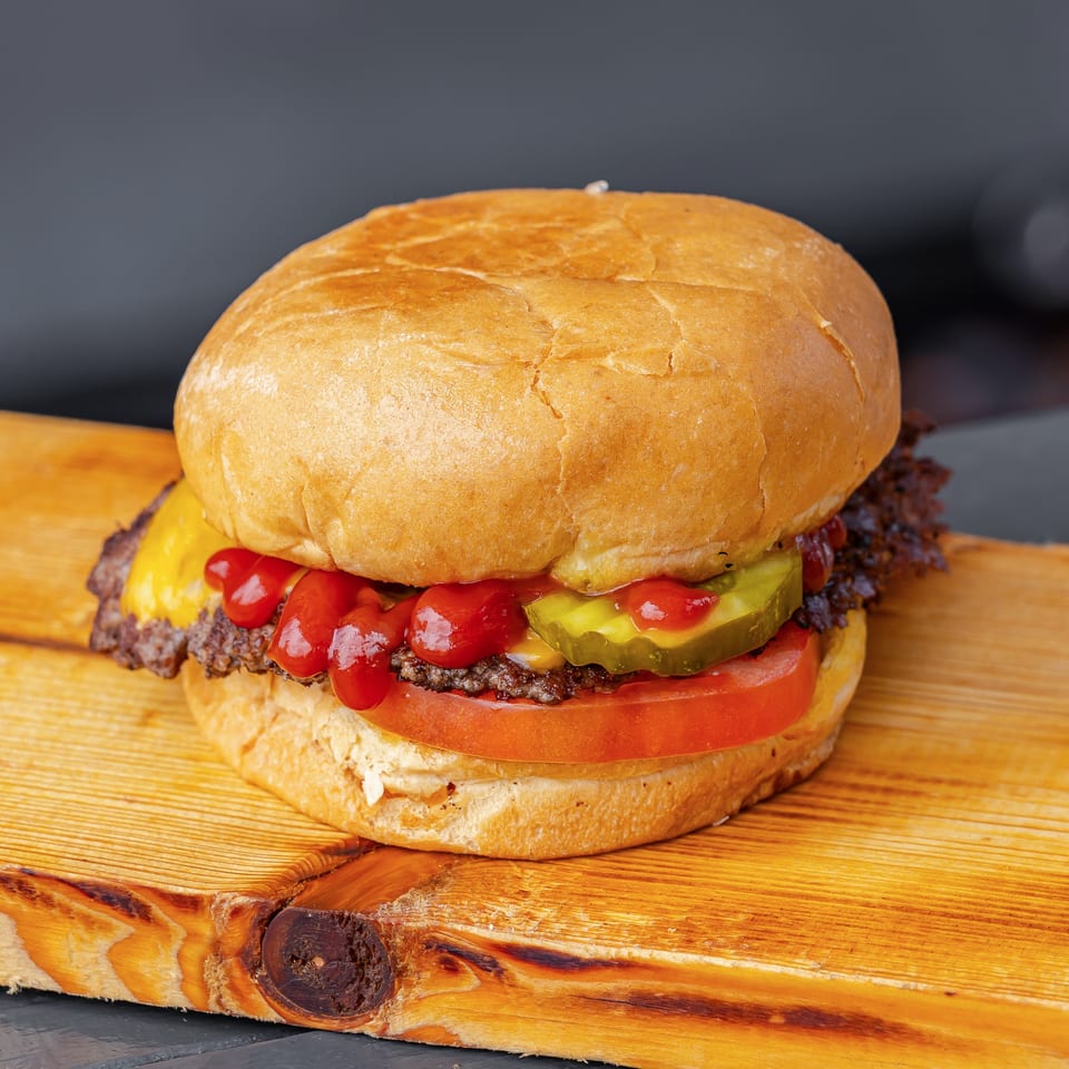 Juicy cheeseburger with pickles, tomato, ketchup, and lettuce on a rustic wooden serving board.