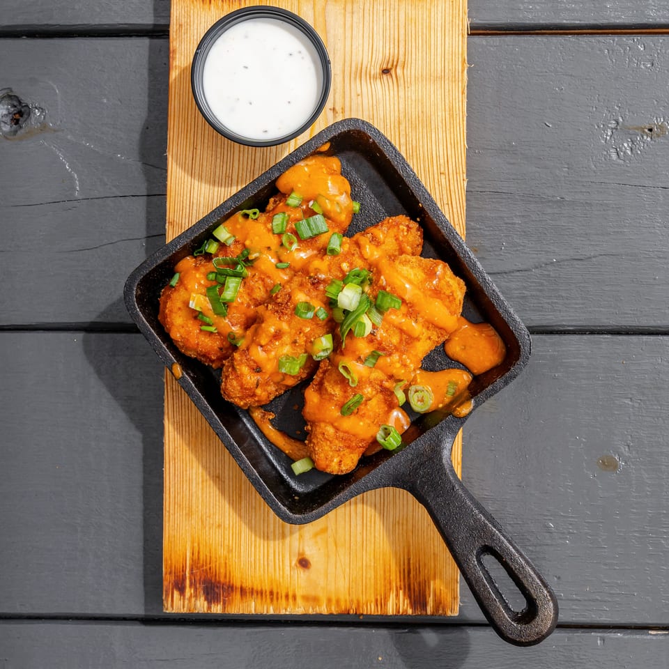 Crispy chicken pieces coated in orange sauce and green onions, served in a cast-iron skillet with ranch dressing.