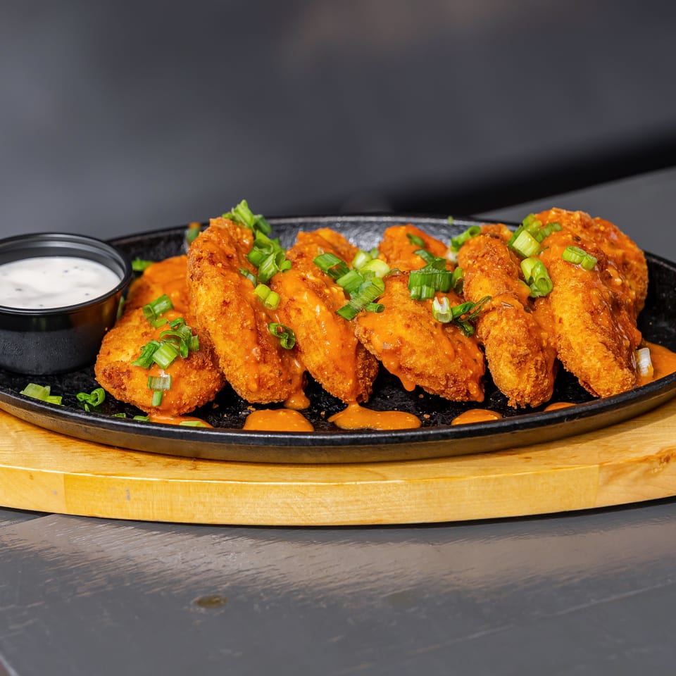 Crispy orange-sauced chicken tenders topped with green onions, served on a black platter with ranch dipping sauce.