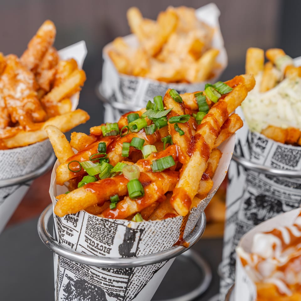Loaded fries topped with spicy sauce and green onions, surrounded by baskets of plain fries and sauced sides.