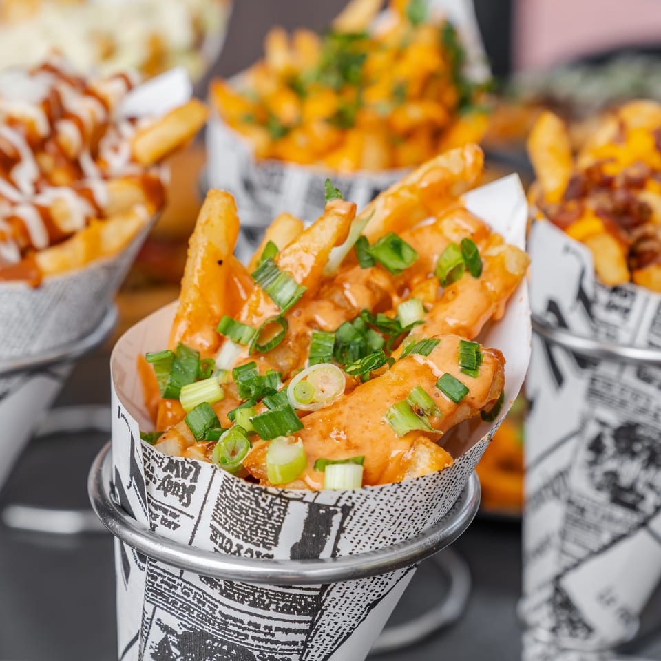 Cups of loaded fries topped with orange sauce, green onions, cheese, and crispy bacon.